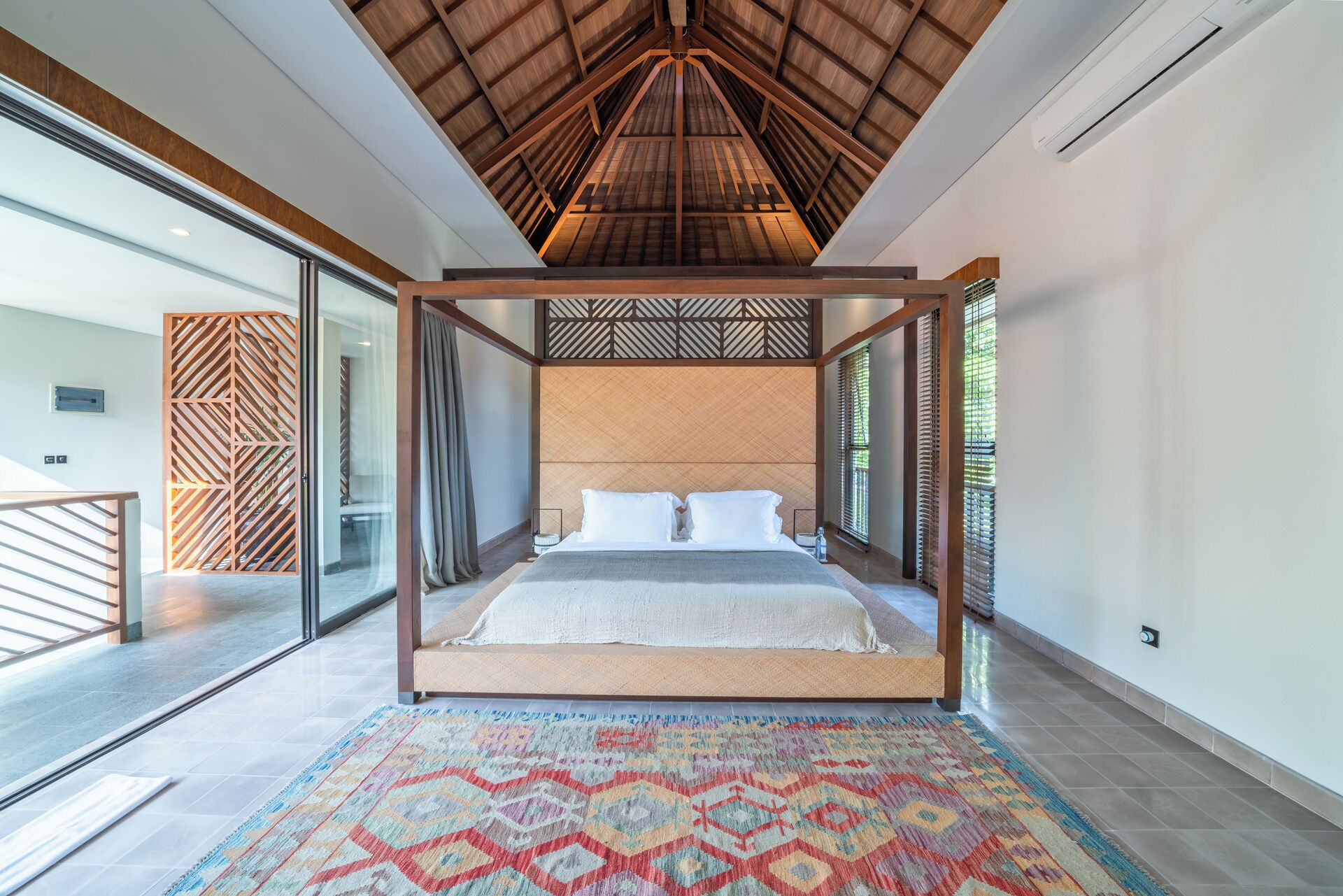 Een moderne slaapkamer met een groot bed, een kamerkleed met een patroon en een houten plafond.
