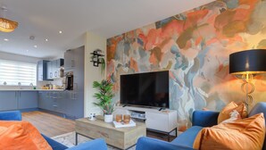 A modern living room with a large flat-screen TV, blue sofas, and a coffee table.