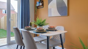 A dining area with a table set for four, chairs, a potted plant, and a wall-mounted shelf with books and a plant.