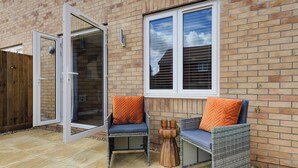 An open sliding glass door leading to a patio area with two wicker chairs and a small wooden table.