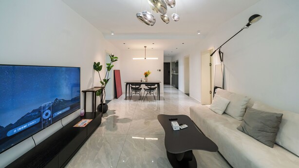 Ein modernes Wohnzimmer mit Flachbildfernseher, Couchtisch, Sofa, Essbereich mit Stühlen und einer Pendelleuchte.
