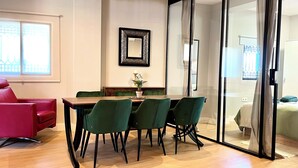 Un espace repas moderne avec une table en bois et des chaises vertes, un canapé rouge et un grand miroir au mur.