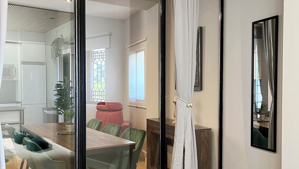Une chambre d’hôtel moderne dotée d’une porte-fenêtre coulissante donnant sur un coin repas, d’un lit avec une serviette bleue et d’un miroir au mur.