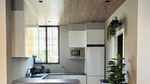 Une cuisine moderne avec un îlot central, un coin repas avec des chaises vertes et une plante en pot sur la table.