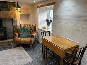 Een gezellige kamer met een leren fauteuil, een houten eettafel en een stenen openhaard.
