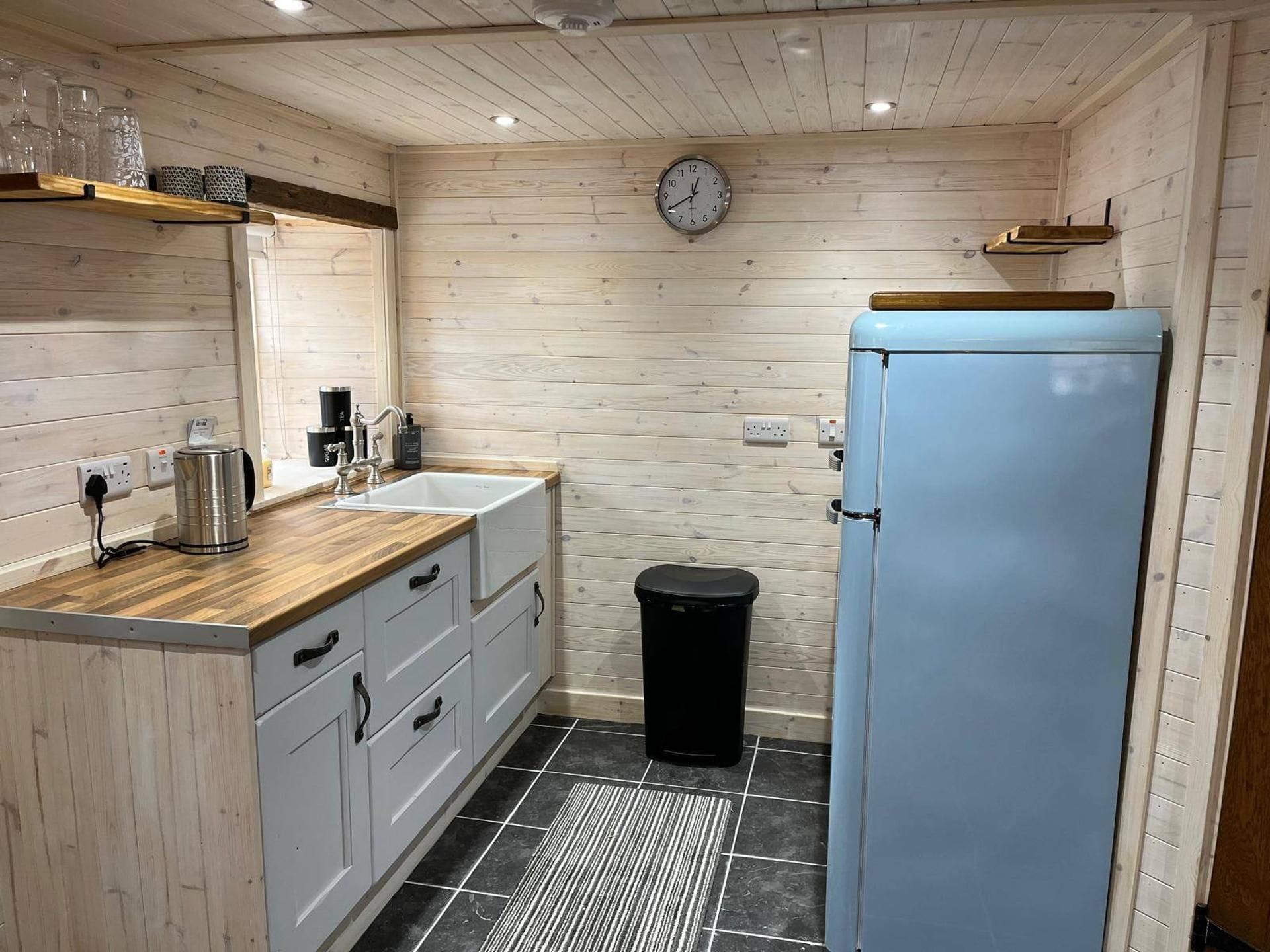 A compact kitchen with a wooden countertop, a sink, a clock, and a blue refrigerator.