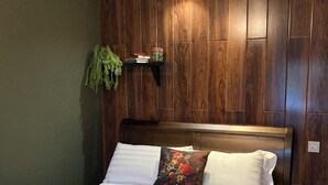 Ein Bett mit weißen Bettwäsche und einer grünen Tagesdecke, ein hölzernes Kopfende und eine kleine Ablage mit Pflanze und Büchern.