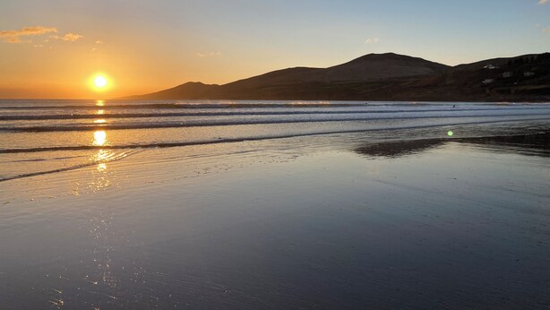 Ein Strand mit Sonnenuntergang, Wellen und fernen Bergen.
