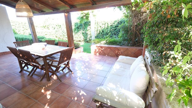 An outdoor patio with a wooden table and chairs, a white sofa, and a hanging light fixture. - Villetta Blu sul Mare a Fontane Bianche by Wonderful Italy (Syracuse)