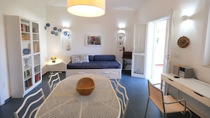 A well-lit room with a bed, a dining table with chairs, a bookshelf, and a desk with a computer. - Villetta Blu sul Mare a Fontane Bianche by Wonderful Italy (Syracuse)