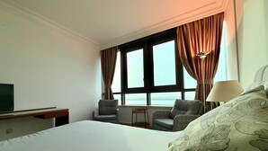 Une chambre d’hôtel avec un grand lit, deux fauteuils, une petite table, un téléviseur et une fenêtre avec des rideaux.