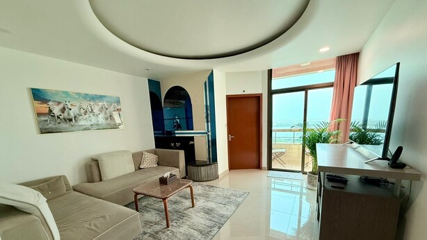 Un salon moderne avec un canapé, une table basse et un tableau. Une porte donne accès à un balcon avec vue.