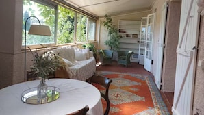 A cozy room with a round table, a sofa, and a chair. There are windows, a door, and a patterned rug.