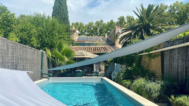 A swimming pool with a white canopy, surrounded by lush greenery and a traditional building in the background.