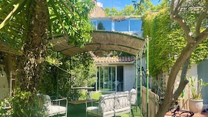 A covered patio with a table and chairs, a small garden area, and a view of a house with a tiled roof.
