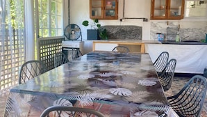A dining area with a glass table, chairs, a fan, and wooden cabinets.