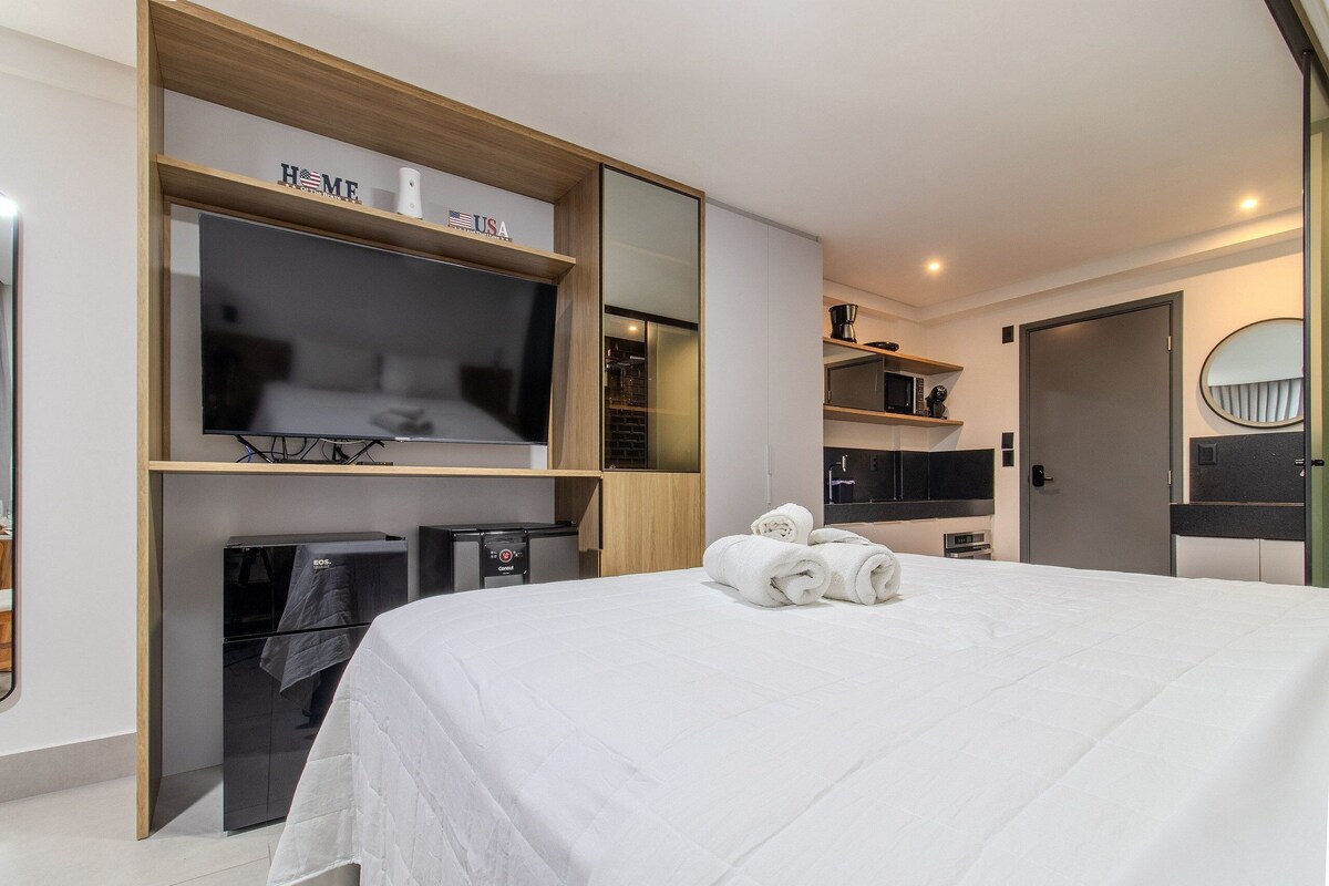 A modern hotel room with a large bed, a flat-screen TV, a minibar, and a built-in wardrobe.