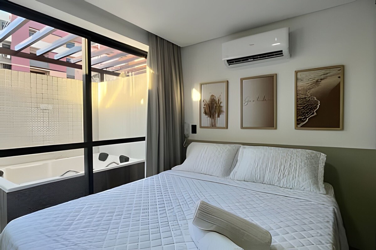 A hotel room with a large bed, an air conditioning unit, and a view through a window to a pool area.