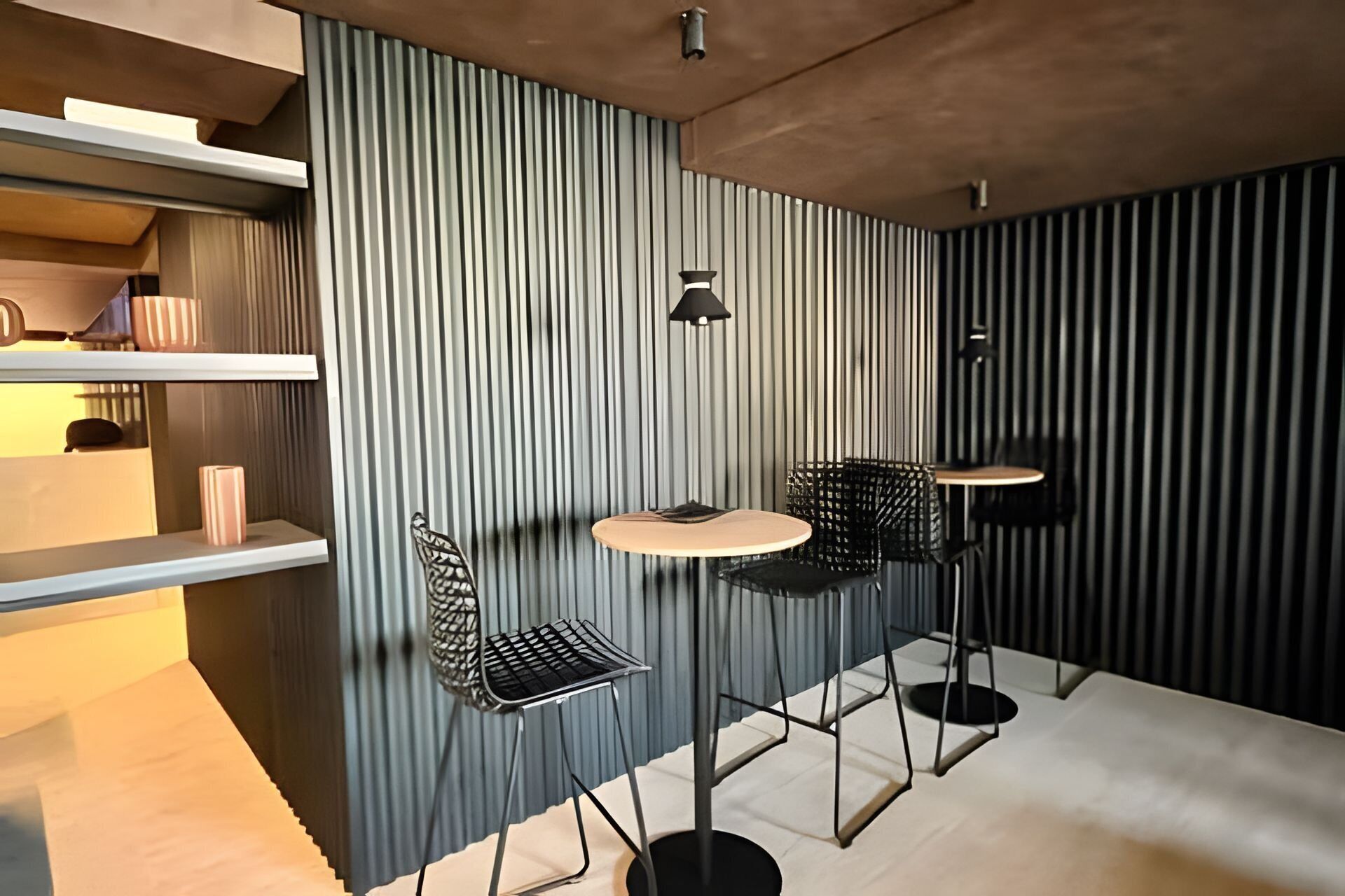 Um interior moderno com parede em listras verticais, uma mesa redonda, duas cadeiras e um lustre suspenso.