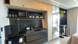 A modern kitchen with a microwave, sink, and cabinets. There is a small refrigerator and a plant on the counter. - Get By Side (João Pessoa)