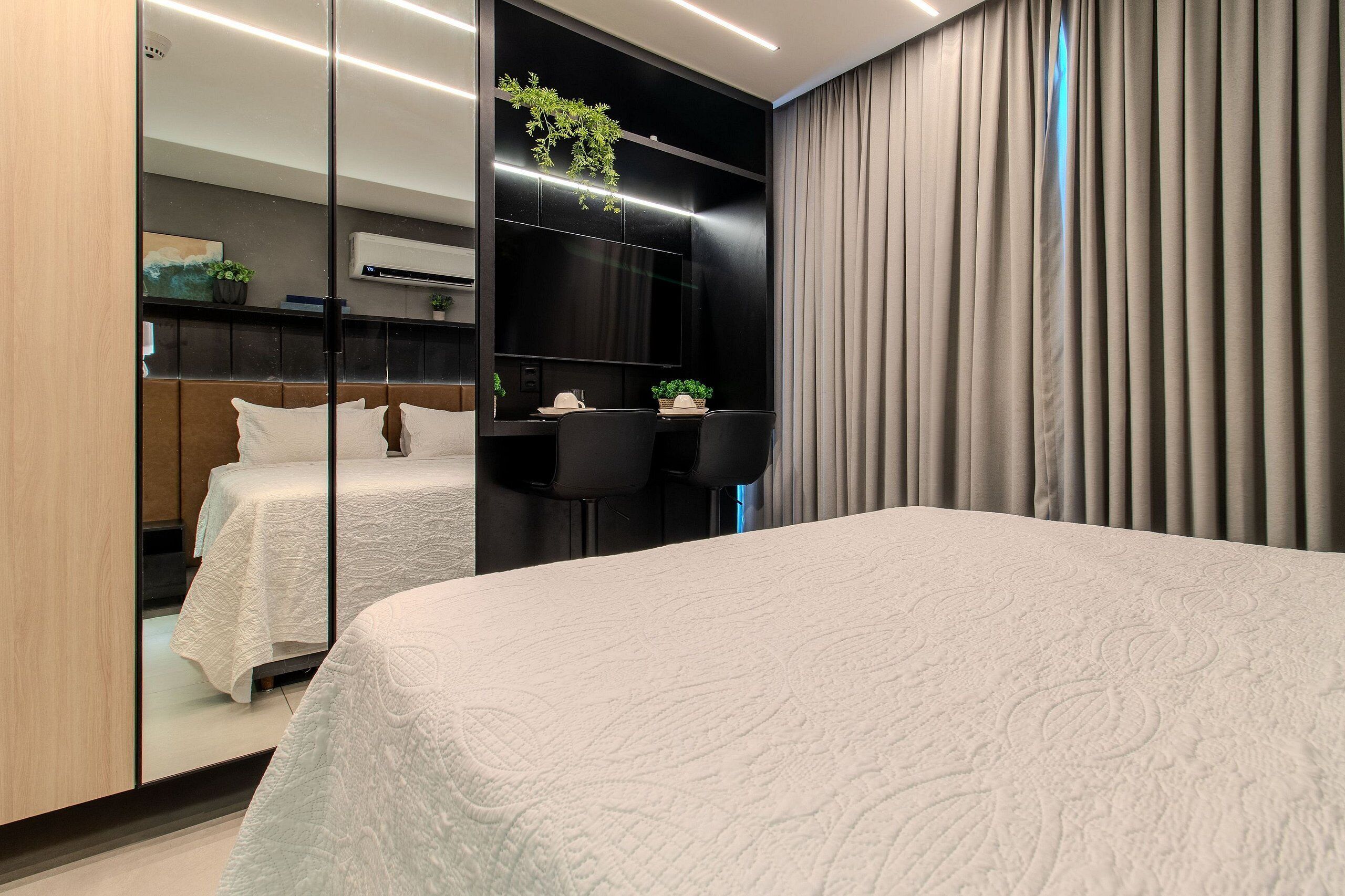 Habitación de hotel moderna con una cama grande, un escritorio con dos sillas, una pequeña mesa con una planta y un espejo amplio.