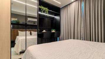 Habitación de hotel moderna con una cama grande, un escritorio con dos sillas, una pequeña mesa con una planta y un espejo amplio.