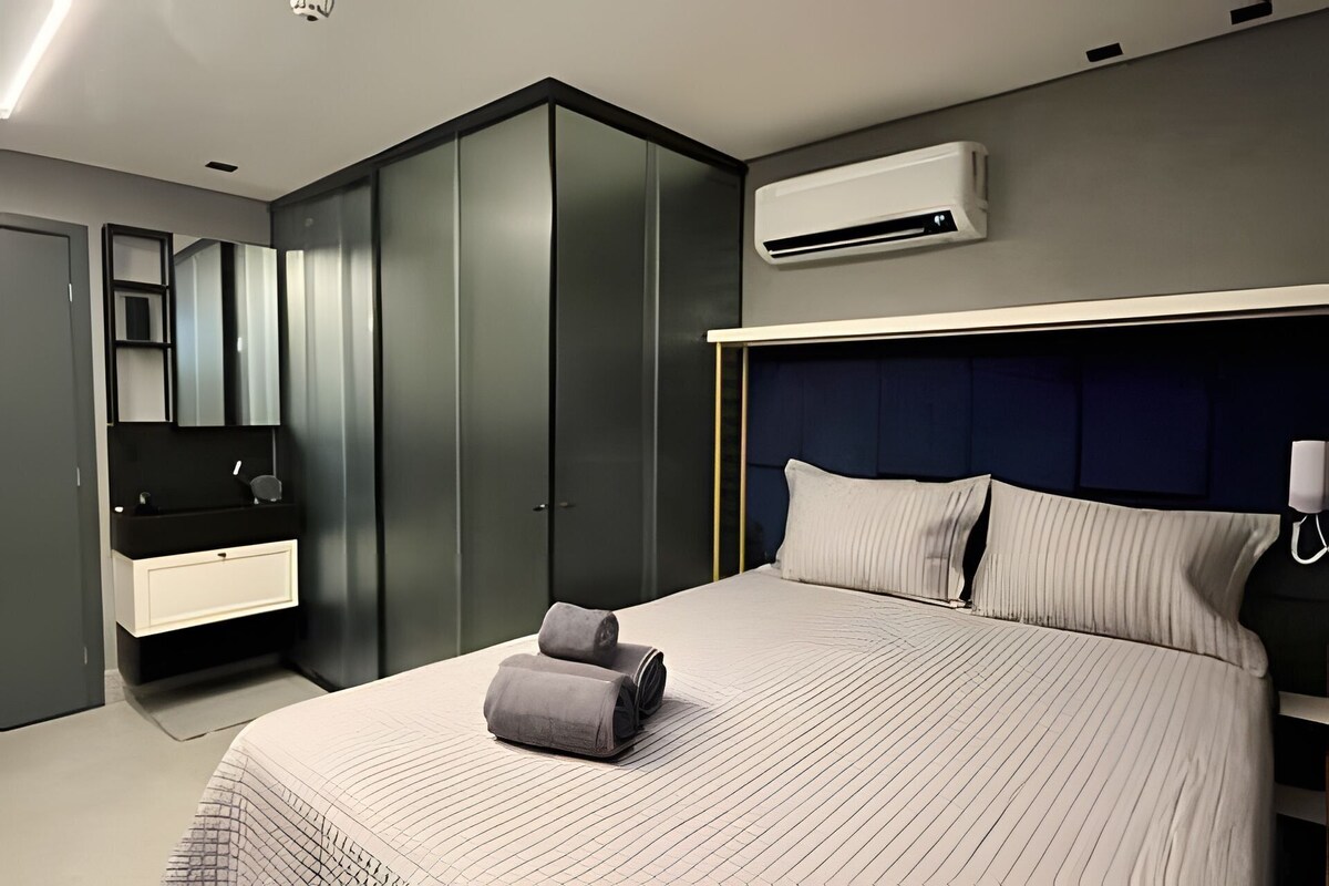A modern bedroom with a bed, bedside tables, a wardrobe, and an air conditioning unit.