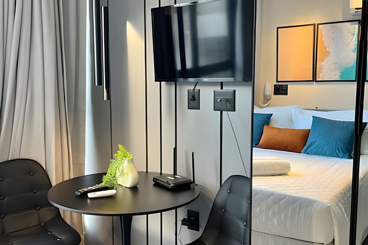 A hotel room with a bed, a TV, a table with a remote control, and a chair.