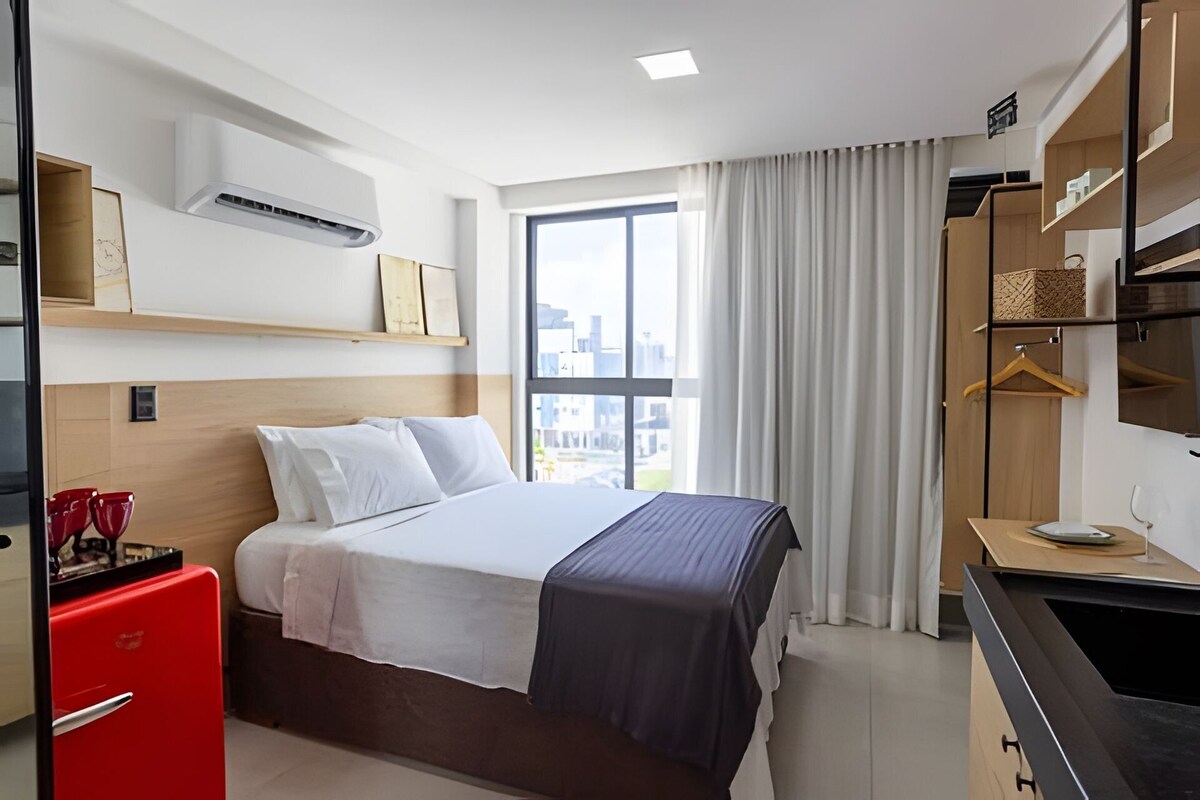 A hotel room with a bed, a red appliance, a wardrobe, and a window with a view.
