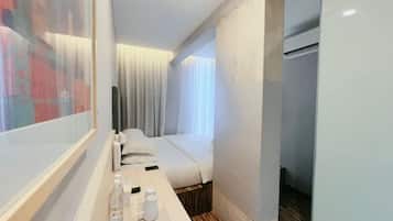 A hotel room with a bed, a bedside table with a bottle and a glass, and a window with curtains.