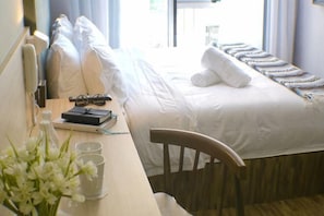 A hotel room with a bed, a desk with a chair, a window, and a bedside table with a bottle and glasses. - Hako Hotel Tun Aminah (Sekudai)