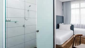 A hotel room with a shower, a bed, a chair, and a window with curtains.