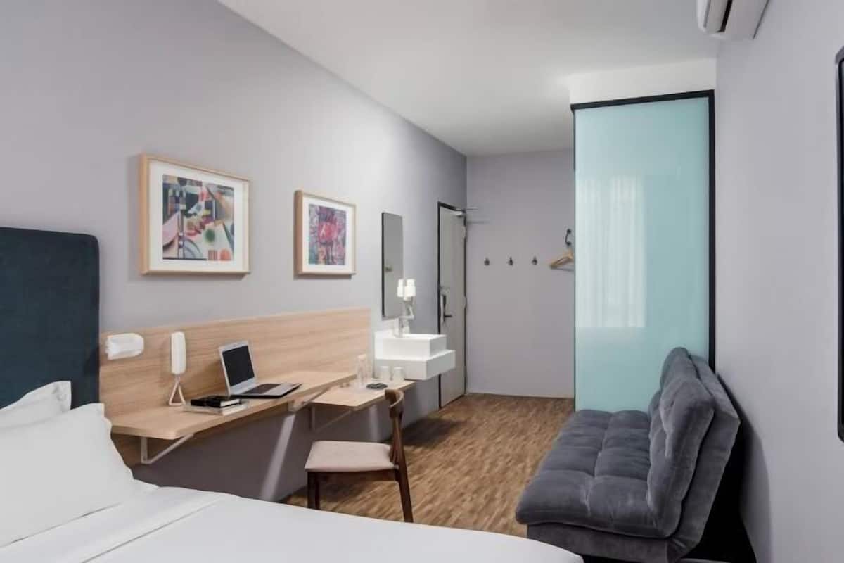 A hotel room with a bed, desk, chair, and a gray couch.