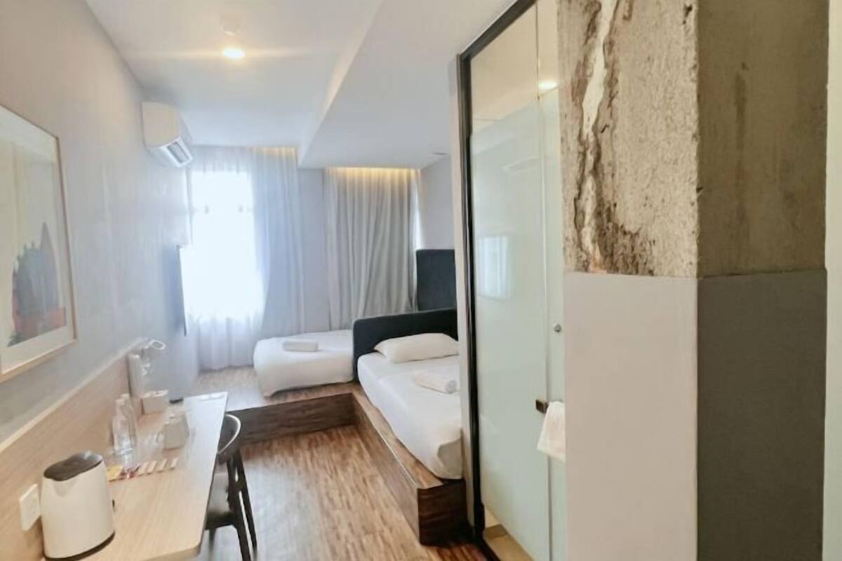 A hotel room with a bed, a desk with a chair, a small table, and a wall-mounted TV.