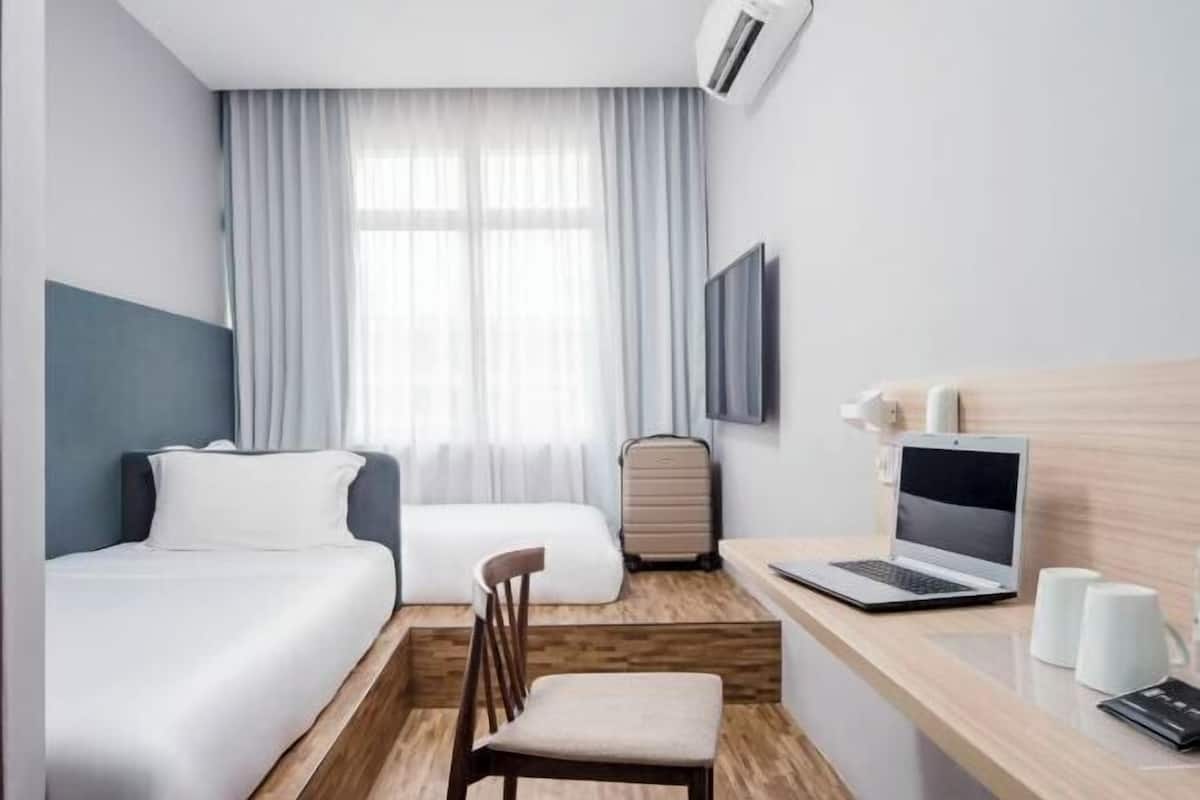 A hotel room with a bed, a desk with a laptop, a chair, a suitcase, and a TV on the wall.