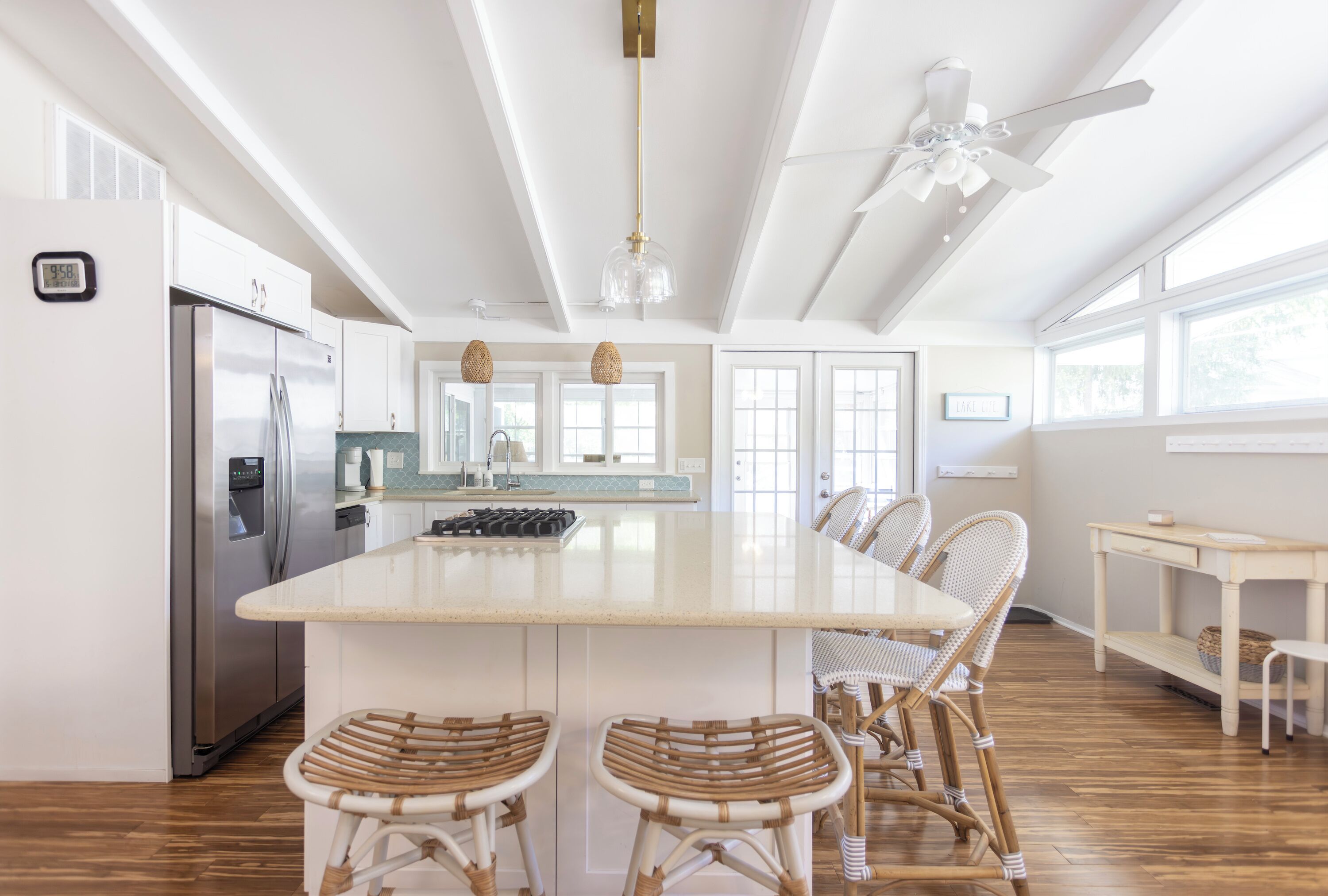 A spacious kitchen with a large island, stainless steel appliances, wicker bar stools, and a ceiling fan.