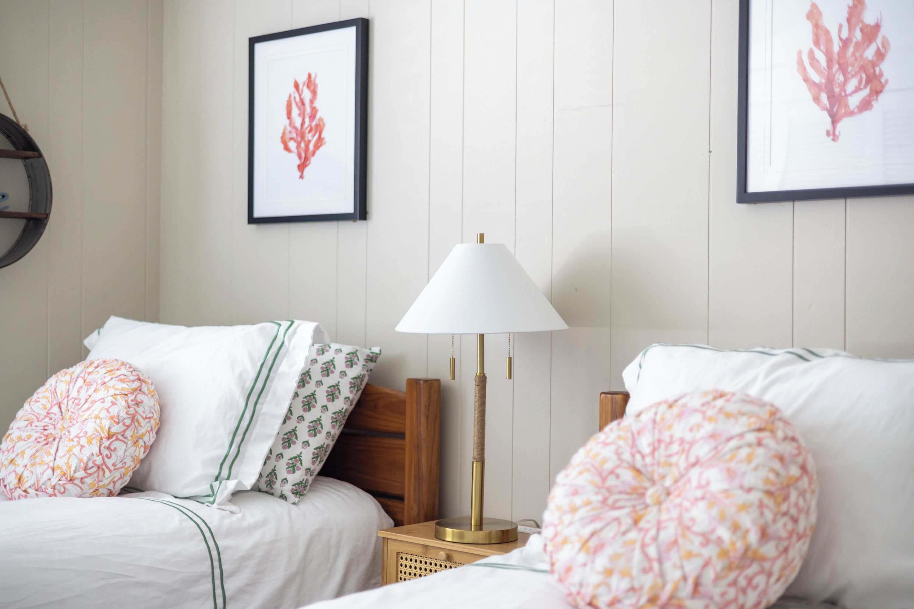 Une chambre d’hôtel bien rangée, avec deux lits, une table de chevet avec une lampe et des œuvres d’art encadrées accrochées au mur.