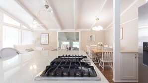 A modern kitchen with a central island, white cabinetry, and a dining area with a wooden table and chairs. - 1000 FT From Lake Michigan, Hot Tub, Golf Cart (Grand Beach)