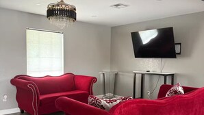 A modern living room with a red sofa, a chandelier, a flat-screen TV, and a large window. - Serene 5-bedroom house with AC in vibrant Houston (Houston)