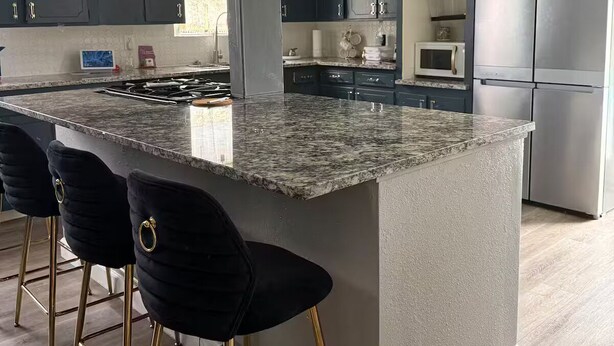 A modern kitchen with dark blue cabinets, a granite countertop, and a stainless steel refrigerator. - Serene 5-bedroom house with AC in vibrant Houston (Houston)