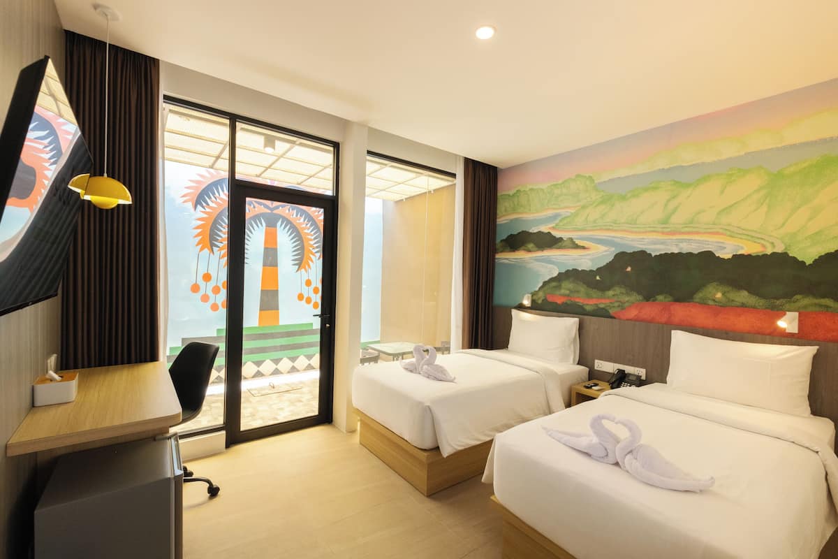Hotelkamer met twee bedden, een bureau, een stoel, een schilderij aan de muur en uitzicht door de deur.