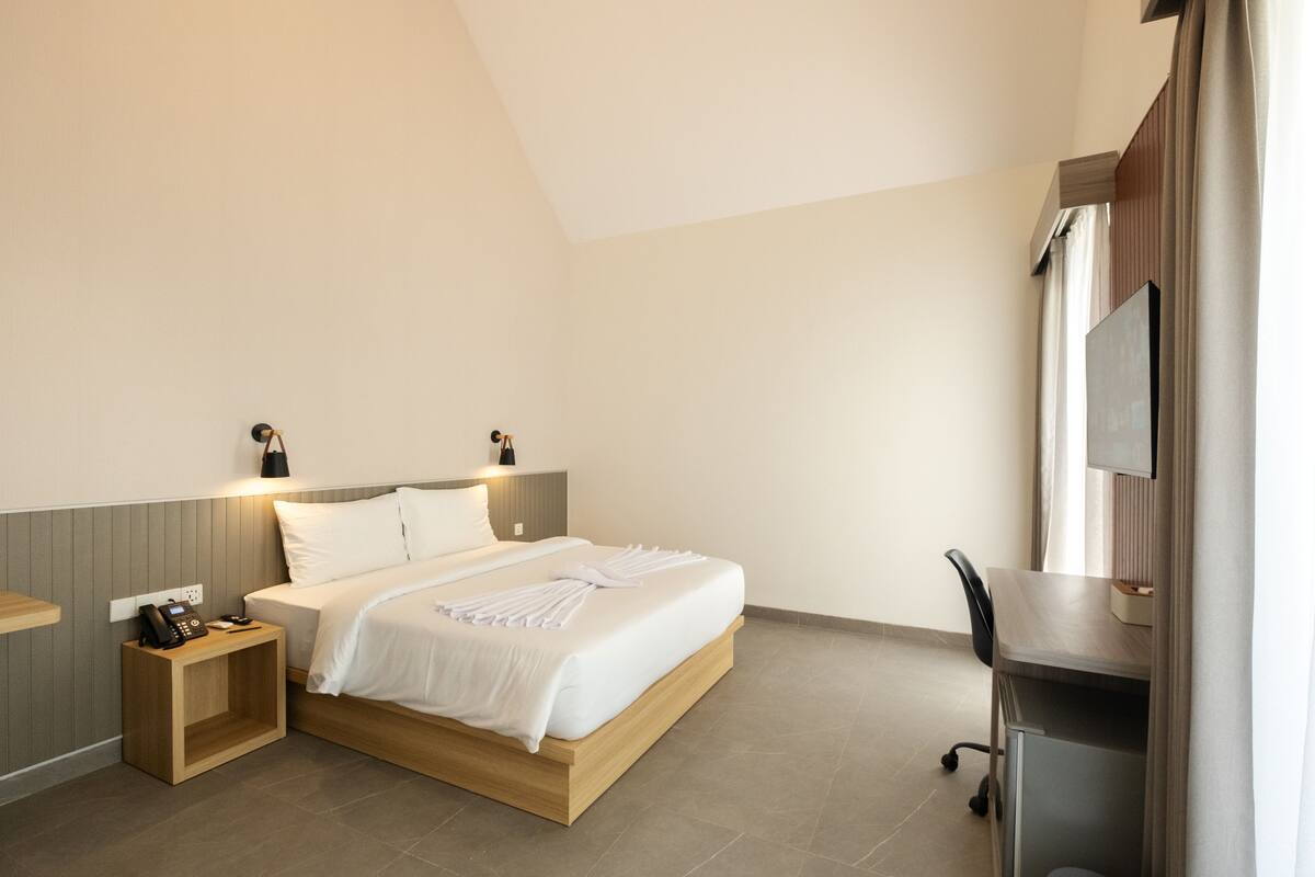 Een moderne hotelkamer met een bed, nachtkastje, bureau en televisie.