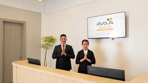 Een receptiegedeelte met een houten receptiebalie, twee personen die erachter staan, een laptop op de balie en een wandmontagescherm waarop de branding 'ayola signature' staat.