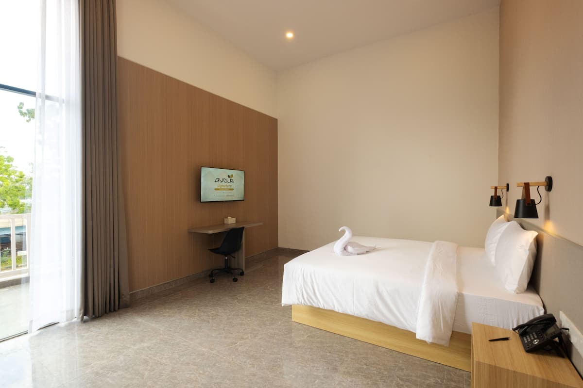Een hotelkamer met een bed, een bureau, een stoel, een aan de muur bevestigde televisie en een raam met gordijnen.