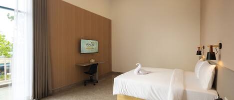 A hotel room with a bed, a desk, a chair, a TV mounted on the wall, and a window with curtains.