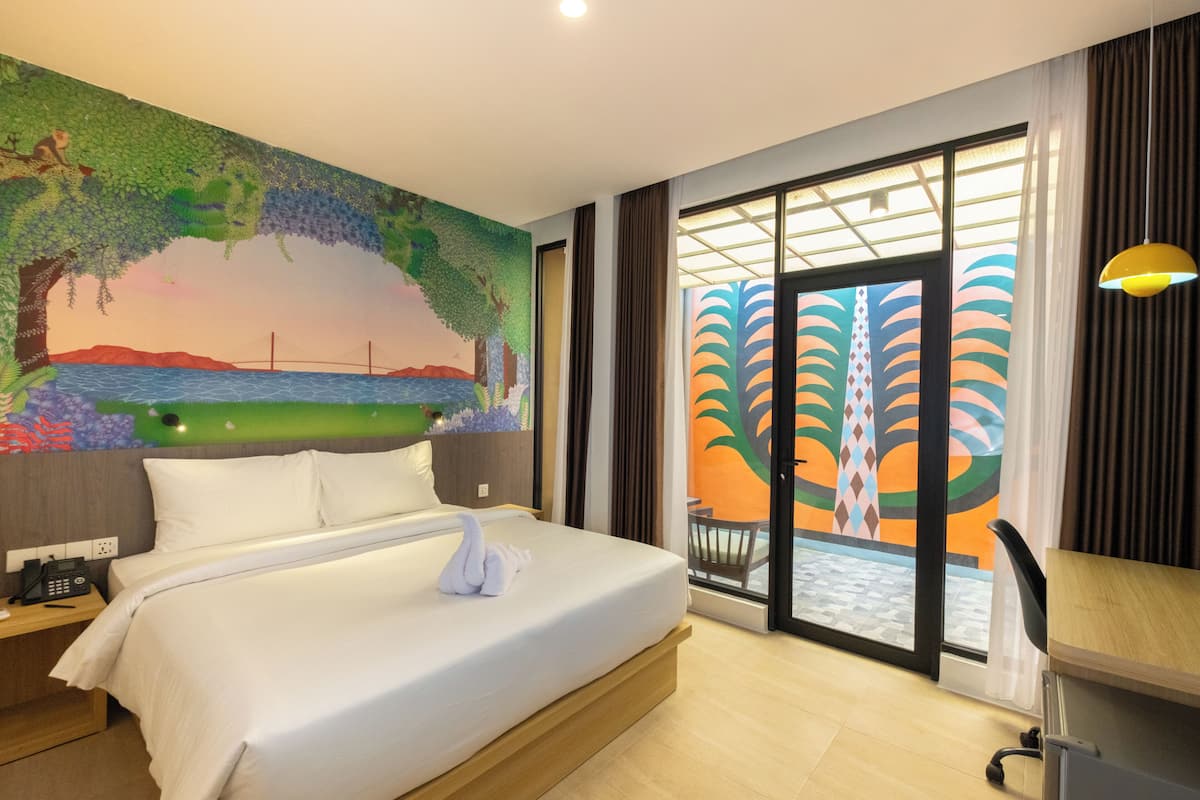 Een hotelkamer met een bed, een bureau, een telefoon en een muurschildering van een landschap.