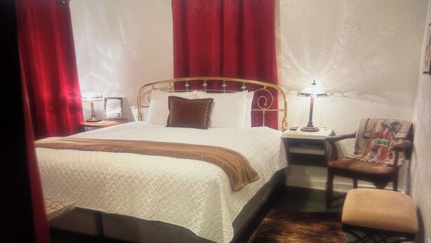 Une chambre à coucher bien rangée, avec un lit, une chaise, une table de chevet et une lampe.