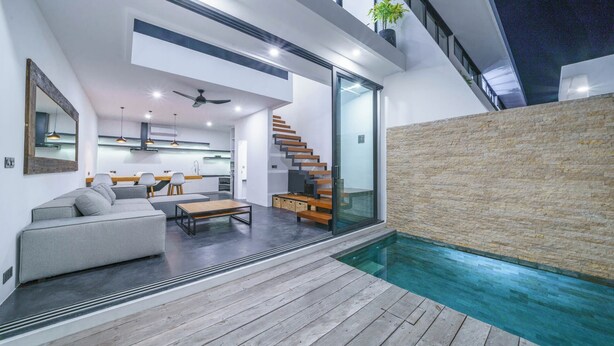Un interior moderno con sala de estar, cocina y escalera que lleva a un balcón.