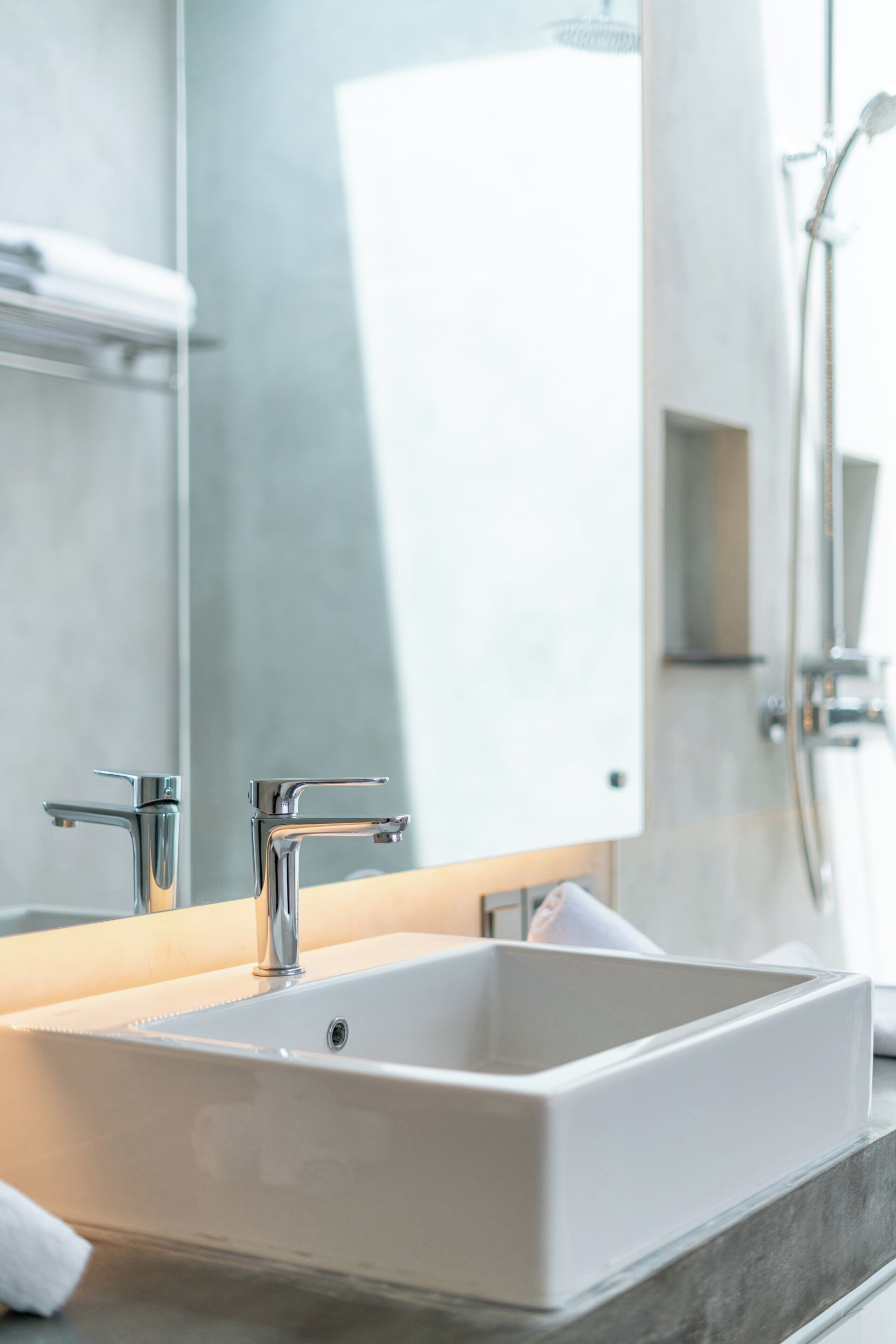 A modern bathroom with a large mirror, a rectangular sink, and a shower area.