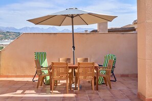 A terrace with a table and chairs, an umbrella, and a view of mountains.